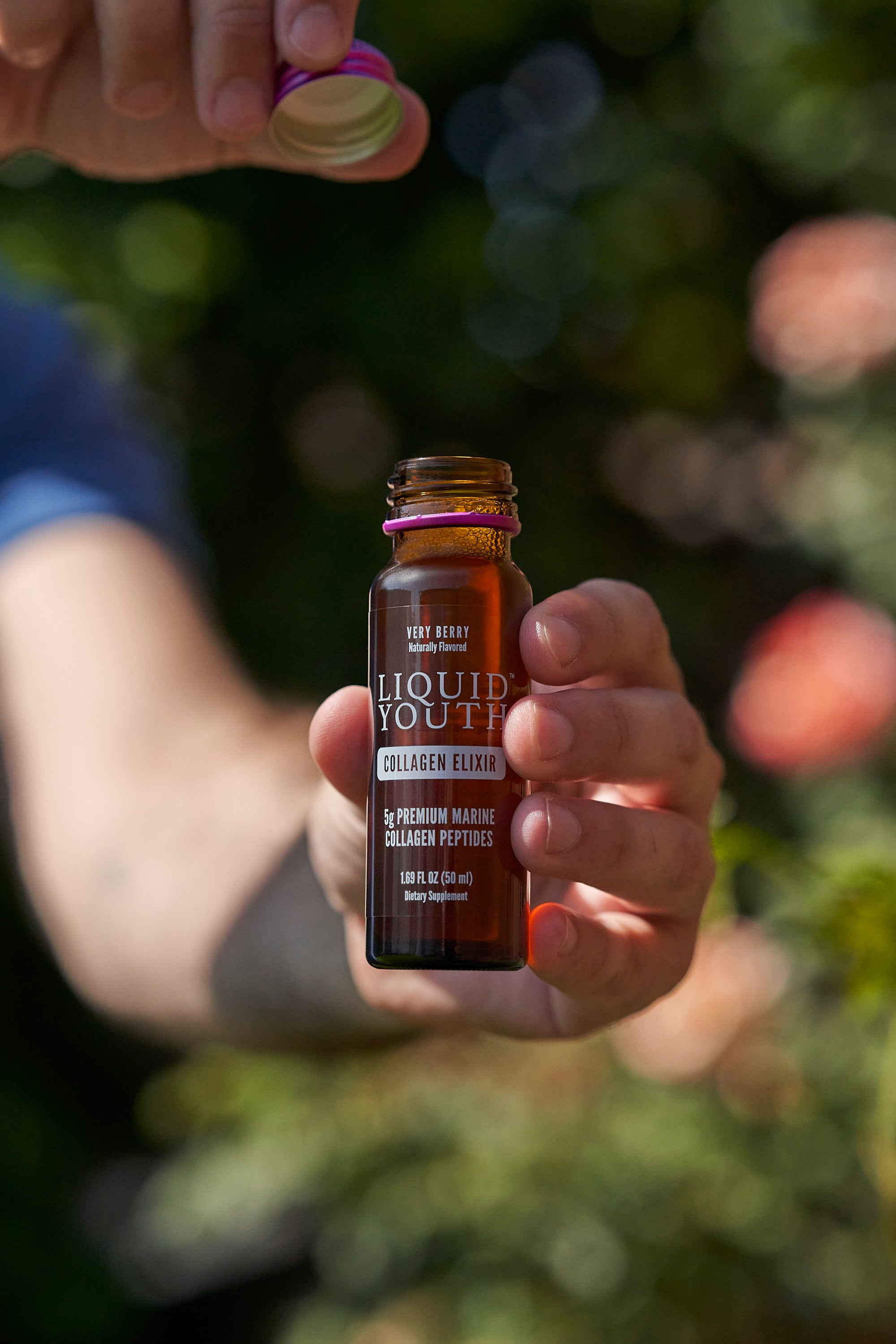 Hand holding an open amber Liquid Youth Collagen Peptide Elixir jar in front of a natural background