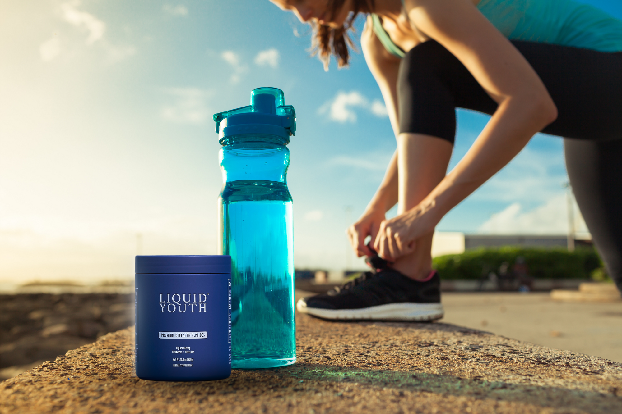 Lady tying her show before a run with her water bottle and Liquid Youth Collagen Peptides near her.